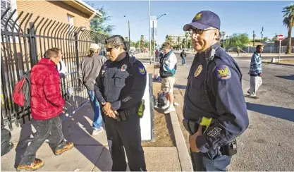  ?? TOM TINGLE/THE REPUBLIC ?? Phoenix police Officers Esteban Navarrette (left) and Lee Williams survey homeless people at 12th Avenue and Madison Street in downtown Phoenix. Central Arizona Shelter Services has opened a parking lot there where the homeless can sleep.