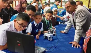  ??  ?? Bright young minds:
Dr Zambry (right) watching the pupils program a robot at the Perak State Library.