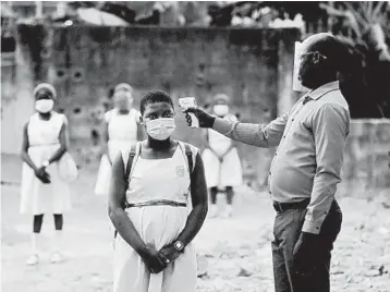  ?? SUNDAY ALAMBA/AP ?? A teacher checks students for fever last month in Nigeria. About 34,000 COVID-19 deaths have been confirmed in Africa.