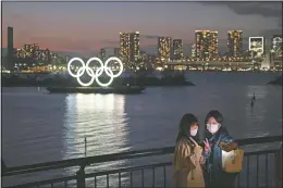  ?? (File Photo/AP/Jae C. Hong) ?? Two women take a selfie March 12, 2020, with the Olympic rings in the background in the Odaiba section of Tokyo. Tokyo Governor Yuriko Koike spoke after the World Health Organizati­on labeled the spreading virus a “pandemic,” a decision almost certain to affect the Tokyo Olympics.