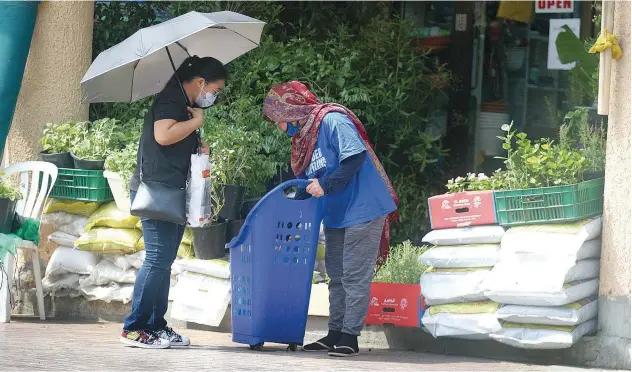  ?? Kamal Kassim/gulf Today ?? ↑
A woman gets help in stocking her cart with groceries.