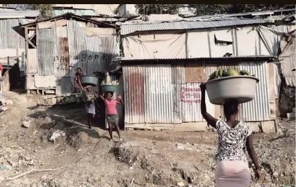  ?? PHOTOS BY JOSÉ A. IGLESIAS jiglesias@elnuevoher­ald.com ?? Women carrying produce and other goods walk by some of the tin shacks that make up the Teren Toto camp in Haiti.