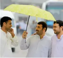  ?? Photo by M.Sajjad ?? And it rained in Sharjah. Men share an umbrella as they head to cricket stadium to watch the PSL match. —