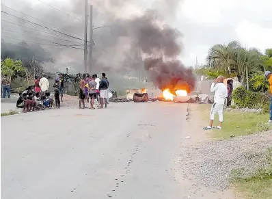  ?? PHOTO BY RUDDY MATHISON ?? Residents look on as debris burns on Terminal Road in Old Harbour Bay, St Catherine, as a protest took place over the police killing of two men yesterday. See story at www.jamaica-gleaner.com.