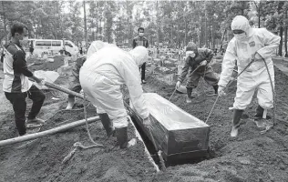  ?? Achmad Ibrahim / Associated Press ?? Workers in protective gear lower a coffin of a COVID-19 victim to a grave for burial at a cemetery in Bogor, Indonesia. The world’s fourth-most populous country has been hit hard by the virus.