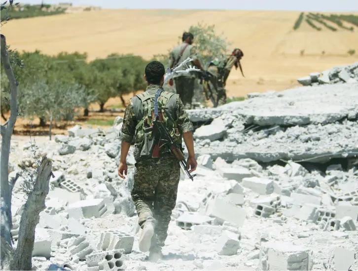  ?? (Reuters) ?? FIGHTERS OF the YPG walk on the rubble of a post that belonged to Islamic State militants, in the western rural area of Manbij, in the Aleppo area. Many volunteers lack new or heavy weapons in the war.