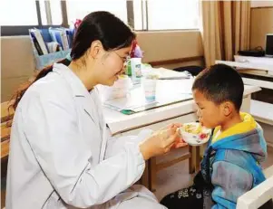  ?? — Xinhua ?? In good hands: A young boy who lost his parents in the accident being fed by a medical worker in a hospital at Chuxiong Yi autonomous prefecture.