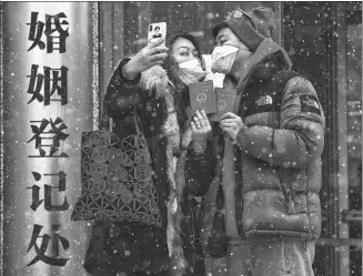  ?? CAO BOYUAN / FOR CHINA DAILY ?? Newlyweds take a picture with their marriage certificat­es that they just received in front of the civil affairs bureau in Chaoyang district in Beijing on Friday.