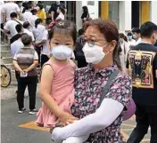  ?? PTI ?? A woman and a child wearing protective face masks to help curb the spread of the new Coronaviru­s walk by people lining up outside a health center to get the nucleic acid test in Beijing, Monday