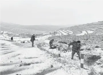  ??  ?? Constructi­on workers shovel dirt onto a road for traction Dec. 16 near a remote mountain village that is part of China’s poverty alleviatio­n program in Gansu province.