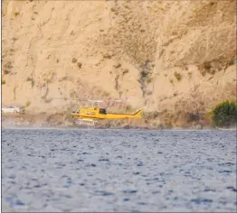  ??  ?? A helicopter attached to the Thomas Creek wildfire fills up with water from Skaha Lake as vehicles pass by on Eastside Road over the weekend.