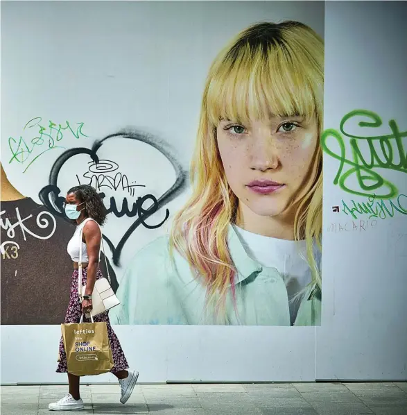  ?? ALBERTO R. ROLDÁN ?? Una mujer pasea con una mascarilla junto a un cartel en una calle del centro de Madrid