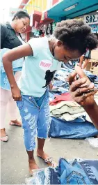  ??  ?? Hyesha Lawrence (left) looks on as her daughter, Tenesha Maxwell, fits a pair of jeans on Orange Street, downtown Kingston, yesterday. Corporal Glenville Sommervill­e directs traffic in downtown Kingston at the corner of Orange and Beckford streets.