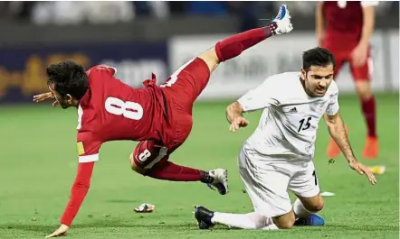  ??  ?? Going down: Qatar’s Ali Assadalla Thaimn (left ) clashes with Iran’s Pejman Montazeri during the World Cup qualifier in Doha on Thursday.