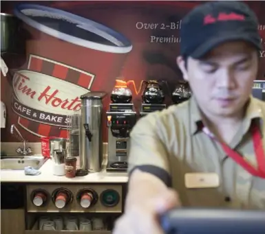  ?? PAWEL DWULIT FOR THE TORONTO STAR/FILE PHOTO ?? The company that owns Tim Hortons plans to extend its global reach. Here, an employee takes an order at a store in Dubai.