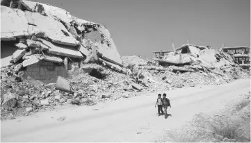  ??  ?? Syrian schoolchil­dren walk past destroyed buildings in a rebel-held area of the southern city of Daraa. — AFP photo