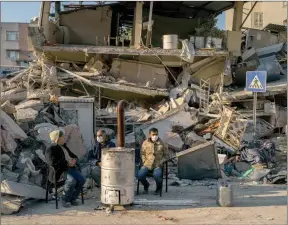  ?? ?? The Associated Press
People sit next to a destroyed house as they wait for the bodies of friends and family members to be pulled from the rubble after an earthquake in Antakya, southeaste­rn Turkey, Monday.