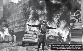  ??  ?? Three cars burn in bright orange flames as a masked protester wearing the signature yellow vest stands in front of them