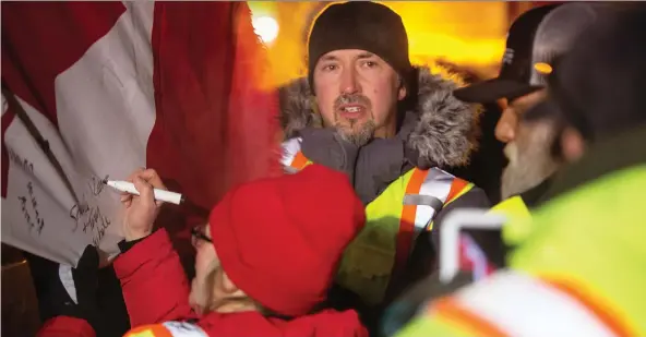  ?? PHOTOS: BRANDON HARDER ?? Rion White of Moose Jaw, centre, stands among the convoy supporters who signed a flag mounted on one of the trucks near Moose Jaw.