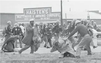  ?? AP FILES ?? A state trooper swings a billy club at John Lewis (right foreground) to break up a civil rights voting march on March 7, 1965, in Selma, Alabama. Lewis suffered a fractured skull.