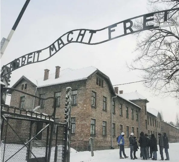  ?? THE ASSOCIATED PRESS ?? Tourists pause near the main entrance and a replica of the inscriptio­n Arbeit Macht Frei (Work Sets You Free) over the entrance to the former Nazi death camp Auschwitz-Birkenau, in Oswiecim, southern Poland. Max Eisen lost 60 family members to the camps.