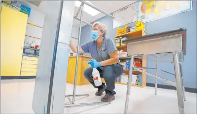  ?? Charlie Neibergall The Associated Press ?? Des Moines Public Schools custodian Cynthia Adams cleans a desk Wednesday in a classroom at Brubaker Elementary School in Des Moines, Iowa. The cost of bringing students back to classrooms is proving a stumbling block to safely reopening schools.