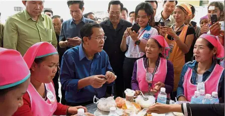  ?? — AFP ?? Staying put: Hun Sen (centre) having lunch and talking with workers at the compound of a factory on the outskirts of Phnom Penh.