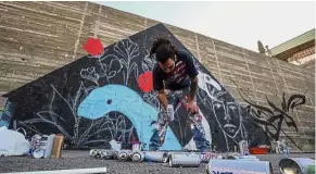  ??  ?? Expression through art: Suhaib picking up a canister of spray paint as he draws a mural on a wall in Amman. — AFP