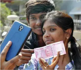  ?? — AFP ?? HYDERABAD: Indian customers pose for a selfie with a new 2,000-rupee currency note at a bank yesterday.