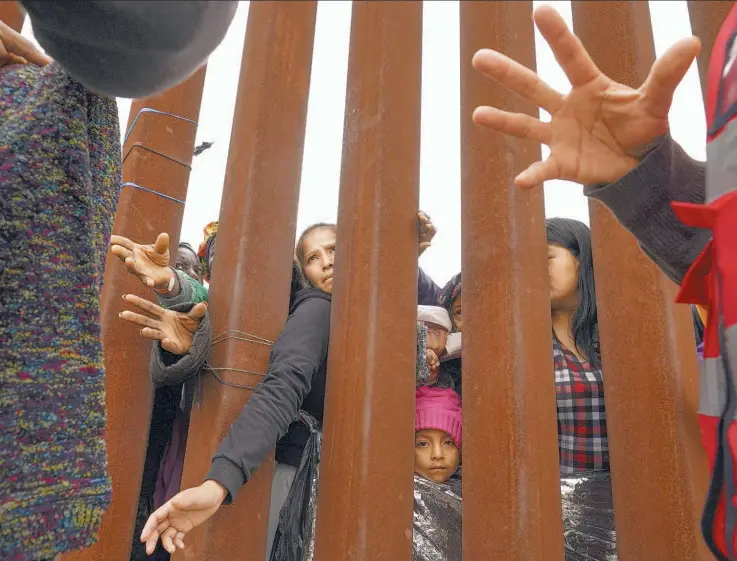  ?? ?? Apoyo entre muros. Migrantes atraviesan un muro fronterizo en busca de ropa entregada por voluntario­s, mientras esperan entre dos fronteras para solicitar asilo en Estados Unidos.