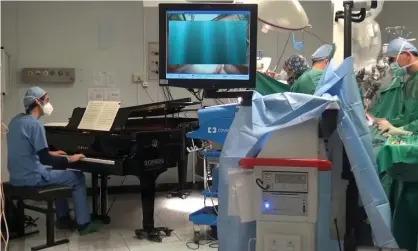  ?? Photograph: Fondazione Salesi/Reuters ?? Roberto Trignani removes a double tumour in the spine of a 10-year-old as molecular biologist Emiliano Toso plays the piano.