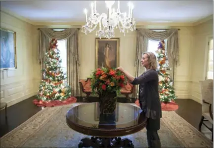  ?? CHUCK KENNEDY — THE WHITE HOUSE — STICHTING KUNSTBOEK VIA AP ?? In this photo provided by Stichting Kunstboek, Laura Dowling completes a holiday arrangemen­t of peach and coral roses in a magnolia leaf vase in the Vermeil Room, before the launch of the White House Christmas season, with the Aaron Shikler portrait of First Lady Jacqueline Kennedy in the background at the White House in Washington. The photograph is featured in the book “Floral Diplomacy: At the White House,” by Laura Dowling.