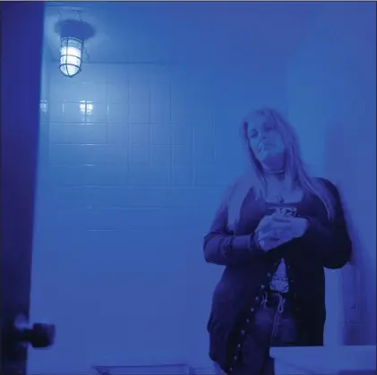  ?? (AP/David Goldman) ?? Misti Mann-France stands for a portrait in a bathroom at the laundromat she manages under a blue light installed to make it harder for drug users to find a vein in Huntington, W.Va. Hers was among several local businesses to install blue lights at the height of the city’s opioid crisis, when they would often find syringes left behind by drug users. “It was the only thing we could think of to do to help,” she said. “And it has helped tremendous­ly.” She said people have overdosed several times in the parking lot of their business, which includes the laundry and a video poker room. A local gas station chain and liquor store also switched to blue lights. “I wish there was a solution to the bigger problem,” she said. “There are so many out there on drugs, and it’s sad, it really is.”