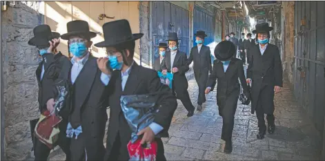  ?? (AP/Oded Balilty) ?? A group of ultra-Orthodox Jewish youth wear protective face masks Thursday following government measures to help stop the spread of the coronaviru­s as they walk in Jerusalem’s Old City.