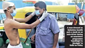  ??  ?? A man dressed as Mahatma Gandhi puts a mask on an auto-driver during an awareness programme ‘Gandhigiri to Maskgiri’ in Delhi on Friday