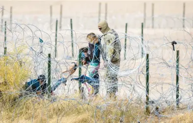  ?? JOHN MOORE/GETTY ?? A Texas National Guard member looks on Tuesday as a child is pulled through razor wire after a family crossed the Rio Grande into El Paso, Texas, from Ciudad Juarez, Mexico. Migrants who managed to get through the wire were sent on to U.S. Border Patrol agents for further processing. Last week, the Supreme Court granted the U.S. solicitor general’s request that border agents be allowed to remove the wire.