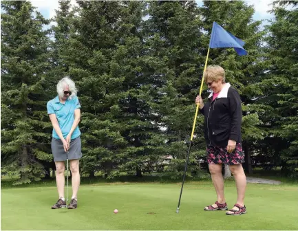  ?? CITIZEN PHOTO BY BRENT BRAATEN ?? Louise Ewen sinks a putt as Ruth Meger holds the flag at Alder Hills Golf Course. Both are co-chairs of the Grandmothe­rs to Grandmothe­rs Prince George golf tournament that takes place Sunday.