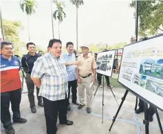  ??  ?? Tengku Adnan (front left) taking a closer look at the constructi­on plan of the multi-storey carpark before the ground-breaking ceremony. — Bernama photo