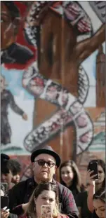  ?? PHOTO/GREGORY BULL ?? People look on in front of a mural depicting heroes of the Mexican revolution during a rally against a scheduled upcoming visit to the area by President Donald Trump on Monday, in San Diego. AP