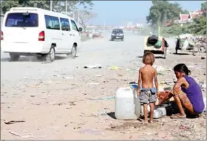  ?? HONG MENEA ?? A woman washes dishes with her son on the side of a dirt road in Phnom Penh’s Daun Penh district.