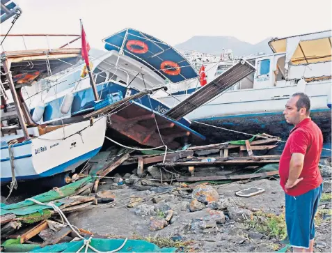  ??  ?? A man looks at damaged boats on a beach in Bodrum, Turkey, following a sea surge caused by the underwater earthquake