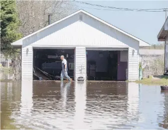  ??  ?? Rick Banks walks past his garage while cleaning up debris at his property along Route 105 in Maugervill­e, N.B.