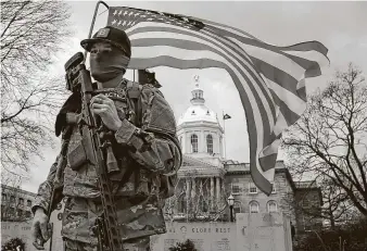  ?? Winslow Townson / Associated Press ?? An armed protester stands in front of the statehouse on Sunday in Concord, N.H. Some statehouse­s were surrounded by new protective fences and had boarded-up windows.