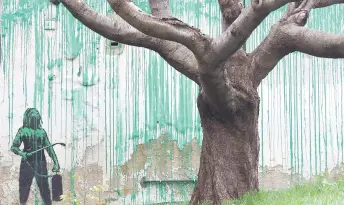  ?? — AFP photos ?? A Banksy artwork is pictured, a stencil of a person having spray painted tree foliage onto a wall behind a leafless tree, a graffiti artwork confirmed as being the work of the famous street artist near Finsbury Park in north London.