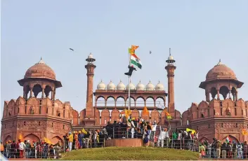  ?? — PTI ?? A farmer hangs on to pole holding a Sikh flag along with a farm union flag outside the historic Red Fort in New Delhi on Tuesday.