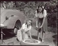  ??  ?? Two young women inflate a car tire with a hand pump, circa 1940-45.