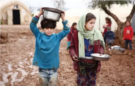  ?? Syrian children carry pots of food at a camp for the displaced near the border with Turkey in the Aleppo province. ??