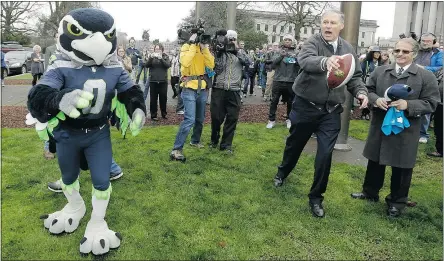  ?? — THE ASSOCIATED PRESS ?? Washington Gov. Jay Inslee, second from right, prepares to pass to Seattle Seahawks mascot Blitz Thursday in Olympia, Wash. Inslee raised a Seahawks flag as part of a rally.