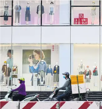  ?? AFP ?? Motorists ride past a Uniqlo store in Hanoi.