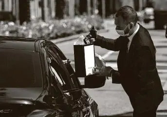  ?? Patrick T. Fallon / Bloomberg ?? An employee wearing a protective mask and gloves hands a purchase to a customer in a vehicle at a curbside pickup outside a Gucci store on Rodeo Drive in Beverly Hills, Calif., on May 19.